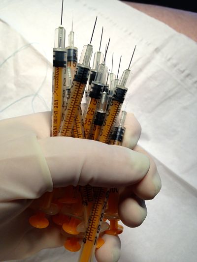 rubber gloved hand holding fist full of needles and syringes preparing for medical role play piercing